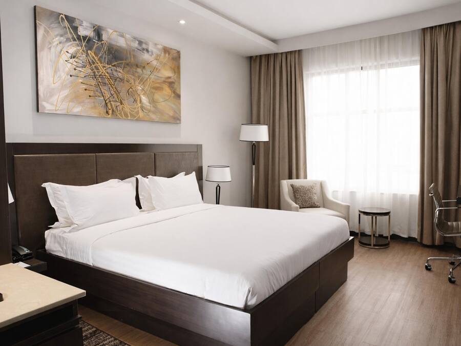 Habitación de hotel con una cama grande, un escritorio, una silla, una lámpara y un cuadro en la pared.