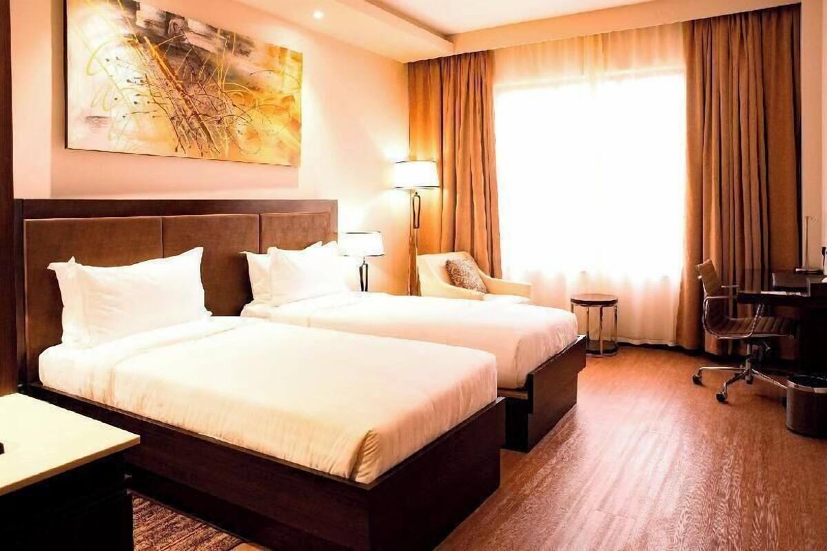 Ein Hotelzimmer mit zwei Betten, einem Schreibtisch, einem Stuhl, einer Lampe und einem Bild an der Wand.