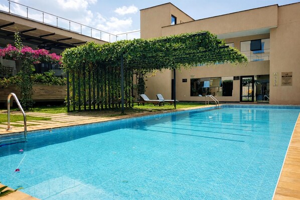A swimming pool with a pergola covered in greenery, lounge chairs, and a building with a modern design in the background. - DoubleTree by Hilton Nairobi Hurlingham (Nairobi)