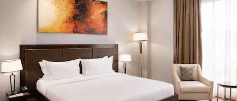 Habitación de hotel con una cama grande, dos mesitas de noche con lámparas, una silla y un cuadro en la pared.