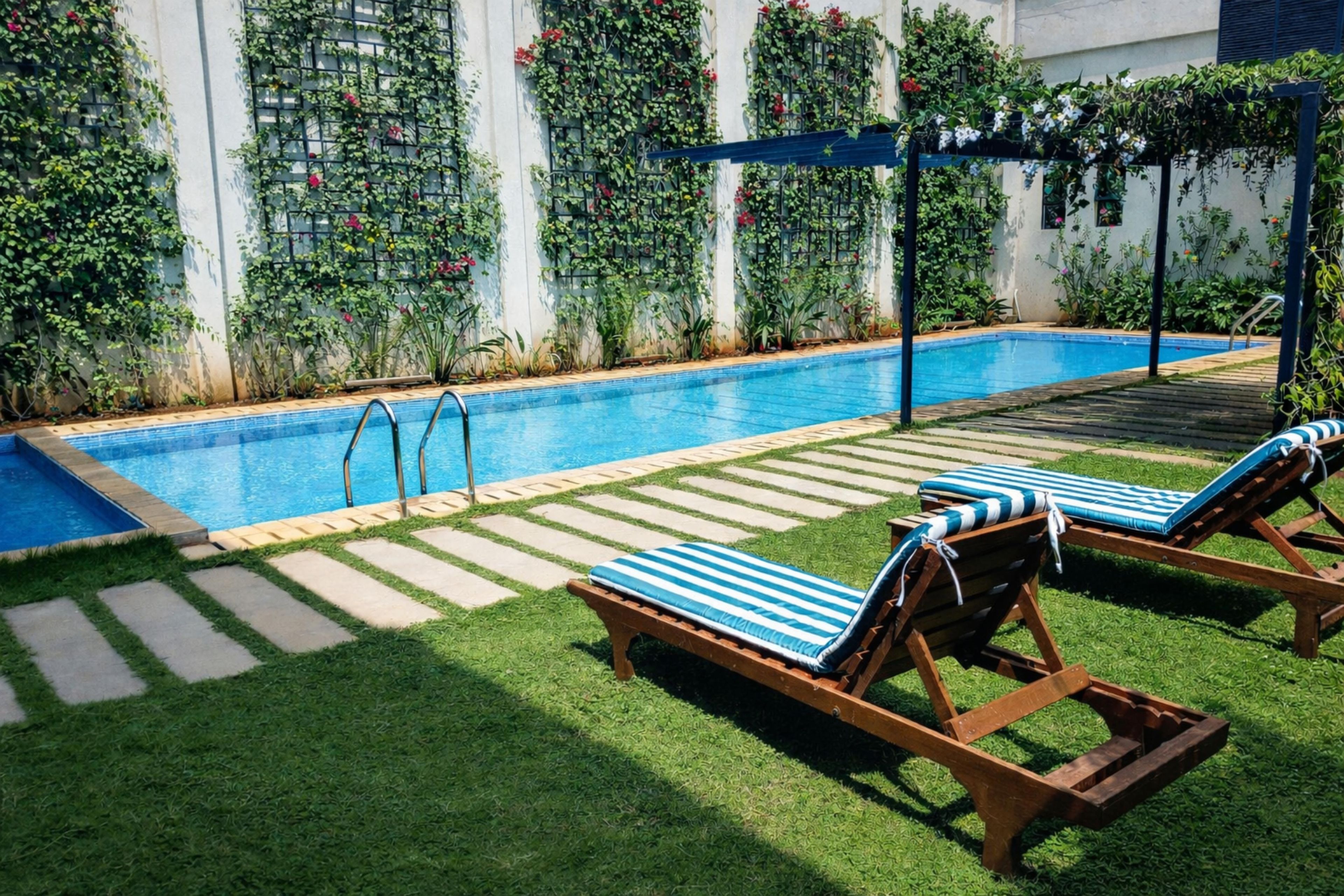Una piscina con dos sillas de descanso, una terraza de madera y un muro de jardín con plantas trepadoras.
