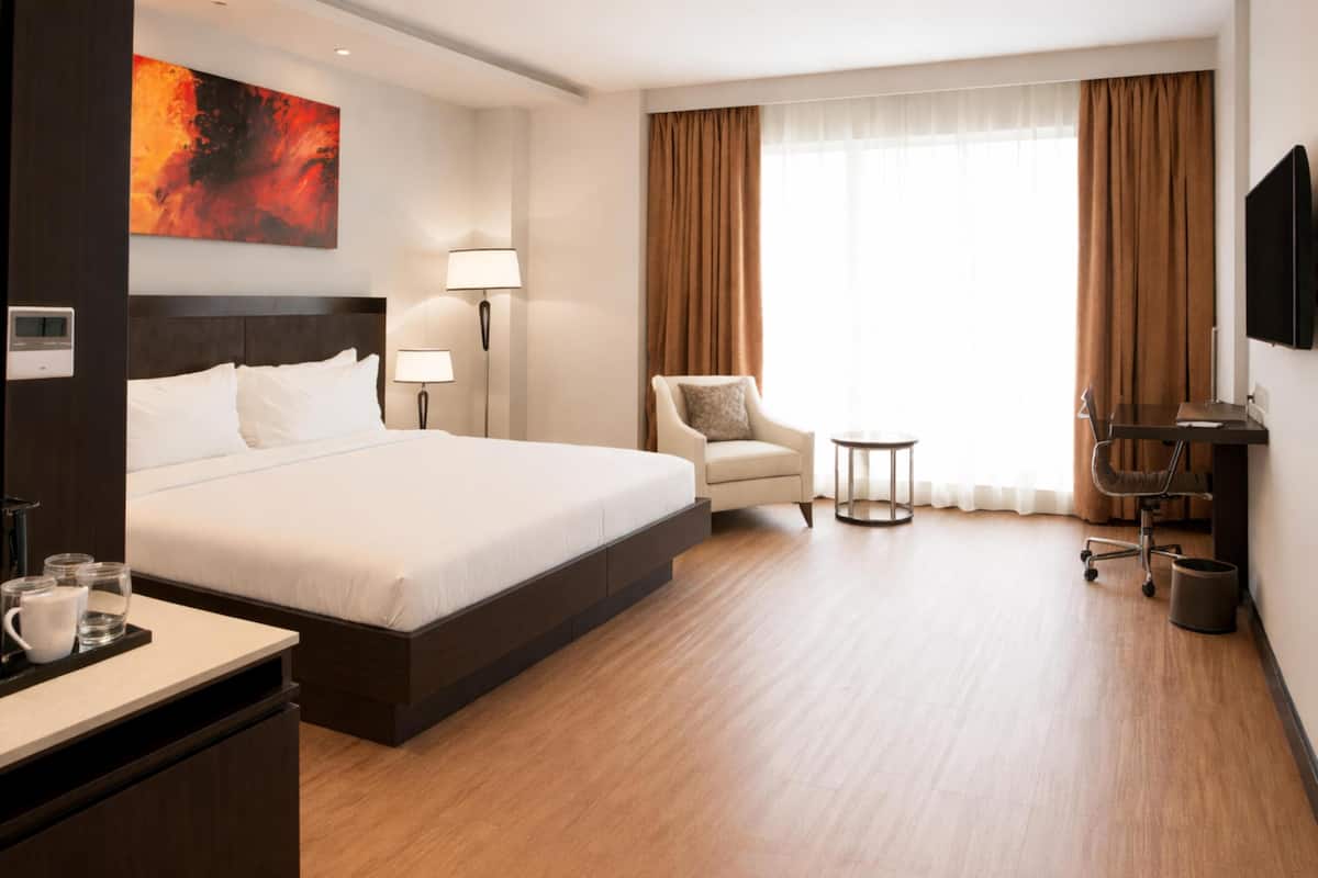 Ein Hotelzimmer mit einem großen Bett, einem Schreibtisch mit Stuhl, einem kleinen Tisch, einer Lampe, einem Fernseher und einem Bild an der Wand.