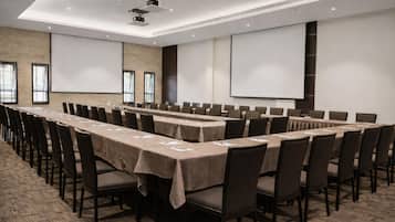 Une salle de conférence équipée de longues tables, de chaises, d’un projecteur et d’écrans.