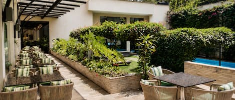 An outdoor patio with wicker furniture, a pool, and lush greenery.