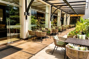 An outdoor seating area with wicker chairs and tables, surrounded by glass walls and potted plants. - DoubleTree by Hilton Nairobi Hurlingham (Nairobi)