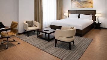 Une chambre d’hôtel avec un grand lit, deux fauteuils, une table basse, un bureau avec une chaise et une lampe.