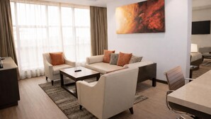 A modern hotel room with a sofa set, a dining table, a TV, and a large abstract painting on the wall. - DoubleTree by Hilton Nairobi Hurlingham (Nairobi)