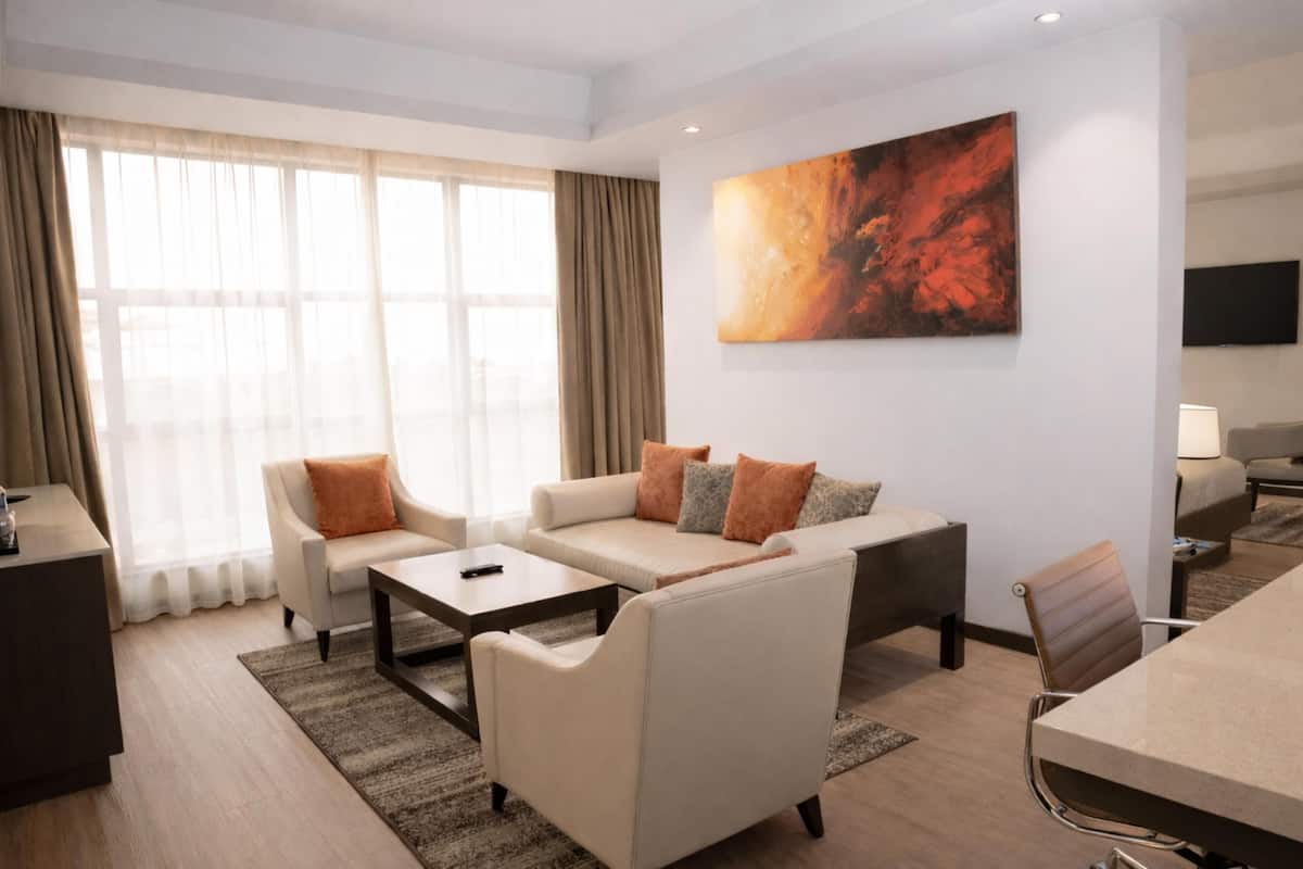 Ein modernes Hotelzimmer mit einer Sofagarnitur, einem Esstisch, einem Fernseher und einem großen abstrakten Gemälde an der Wand.