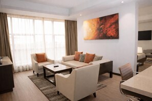 Habitación de hotel moderna con sofá, mesa de comedor, televisor y un cuadro abstracto grande en la pared.