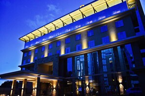 Un hotel de varios pisos con un diseño arquitectónico moderno, destacando un amplio frente de vidrio y un techo plano.
