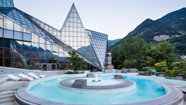 A modern building with a glass facade and a circular pool with a fountain. - La Pleta de Soldeu Apartments (Soldeu)
