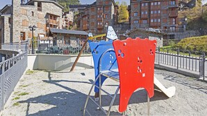 A playground with a slide and climbing structures, surrounded by stone buildings with balconies and a clear sky. - La Pleta de Soldeu Apartments (Soldeu)
