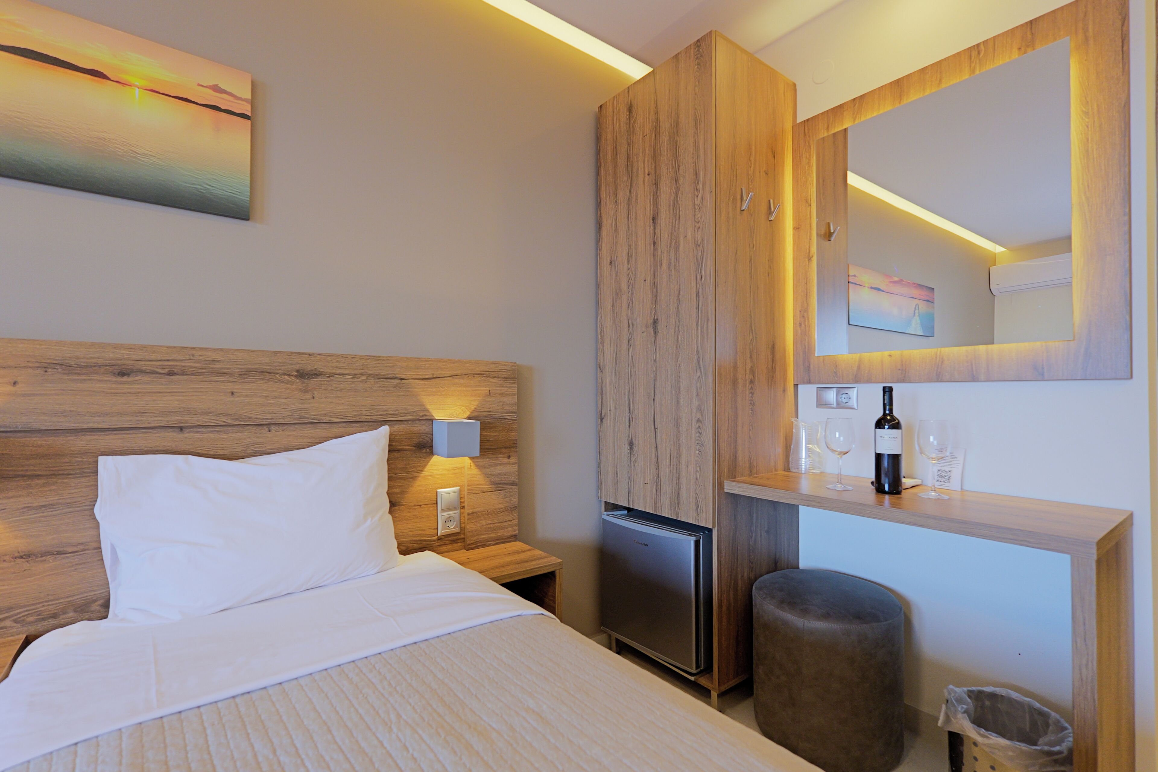Hotelkamer met een bed, een kleine koelkast, een houten kast, een spiegel en een kunstwerk aan de muur.