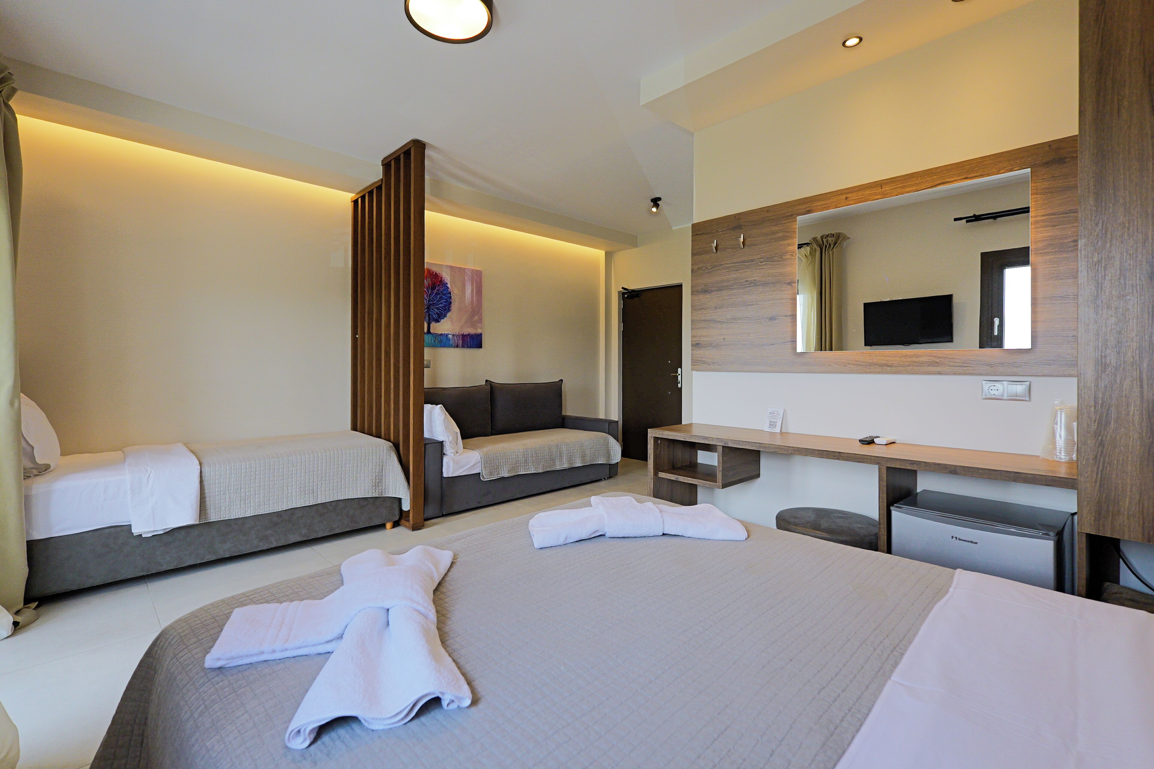 Quarto de hotel moderno com uma cama grande, uma escrivaninha, uma cadeira, uma televisão e um espelho.