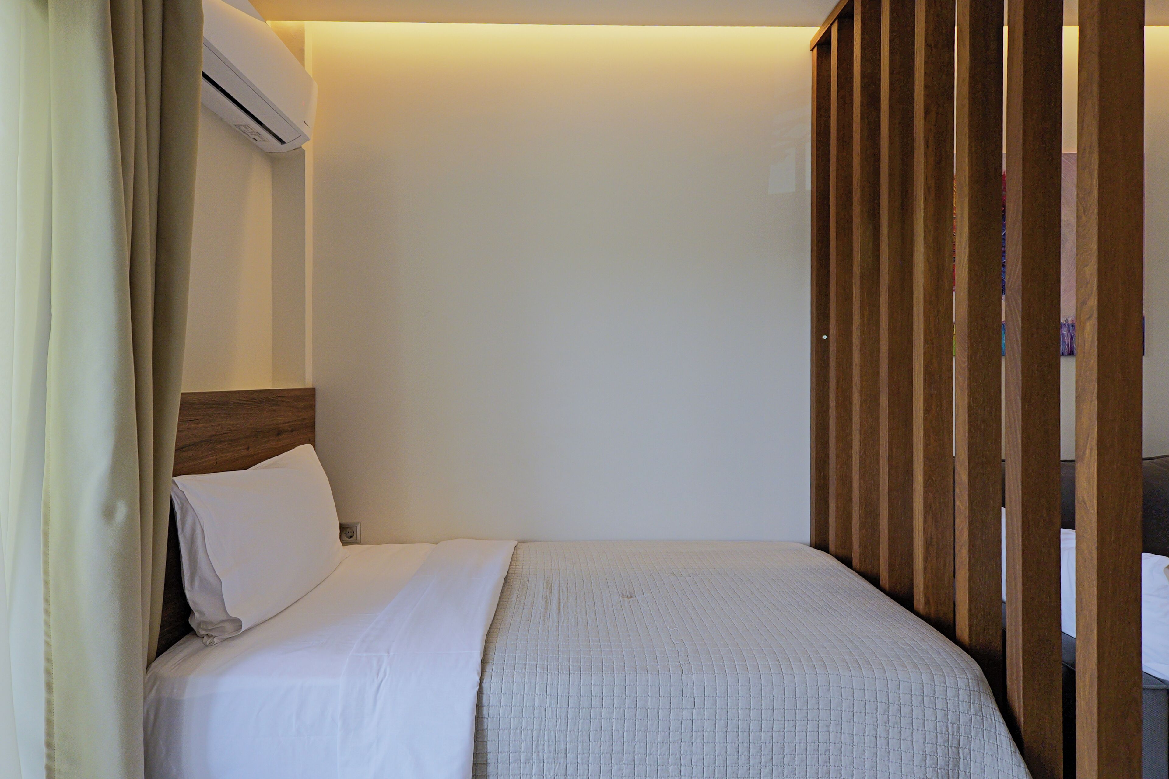 A hotel room with a bed, a wooden headboard, a white wall, and a curtain.