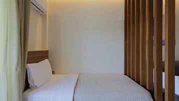 A hotel room with a bed, a wooden headboard, a white wall, and a curtain.