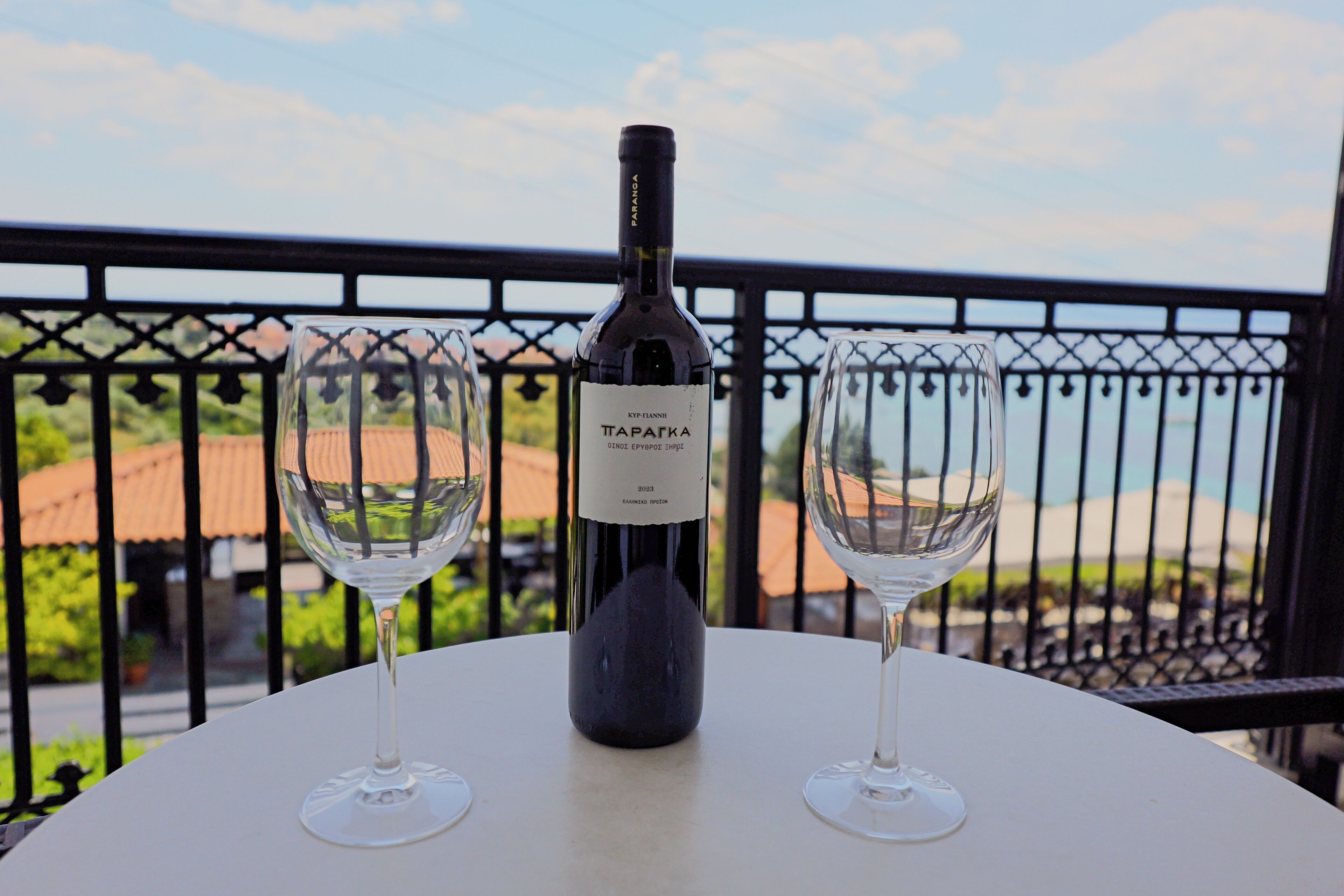 Una botella de vino y dos copas sobre una mesa con vistas a un balcón y edificios.