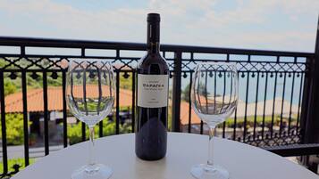 Una botella de vino y dos copas sobre una mesa con vistas a un balcón y edificios.