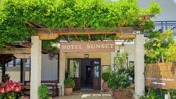 A hotel entrance with a wooden archway, a sign reading 'HOTEL SUNSET,' and potted plants around.