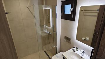 Une salle de bain moderne avec une douche à l’italienne en verre, un lavabo blanc et un miroir agrémenté d’une petite fenêtre.