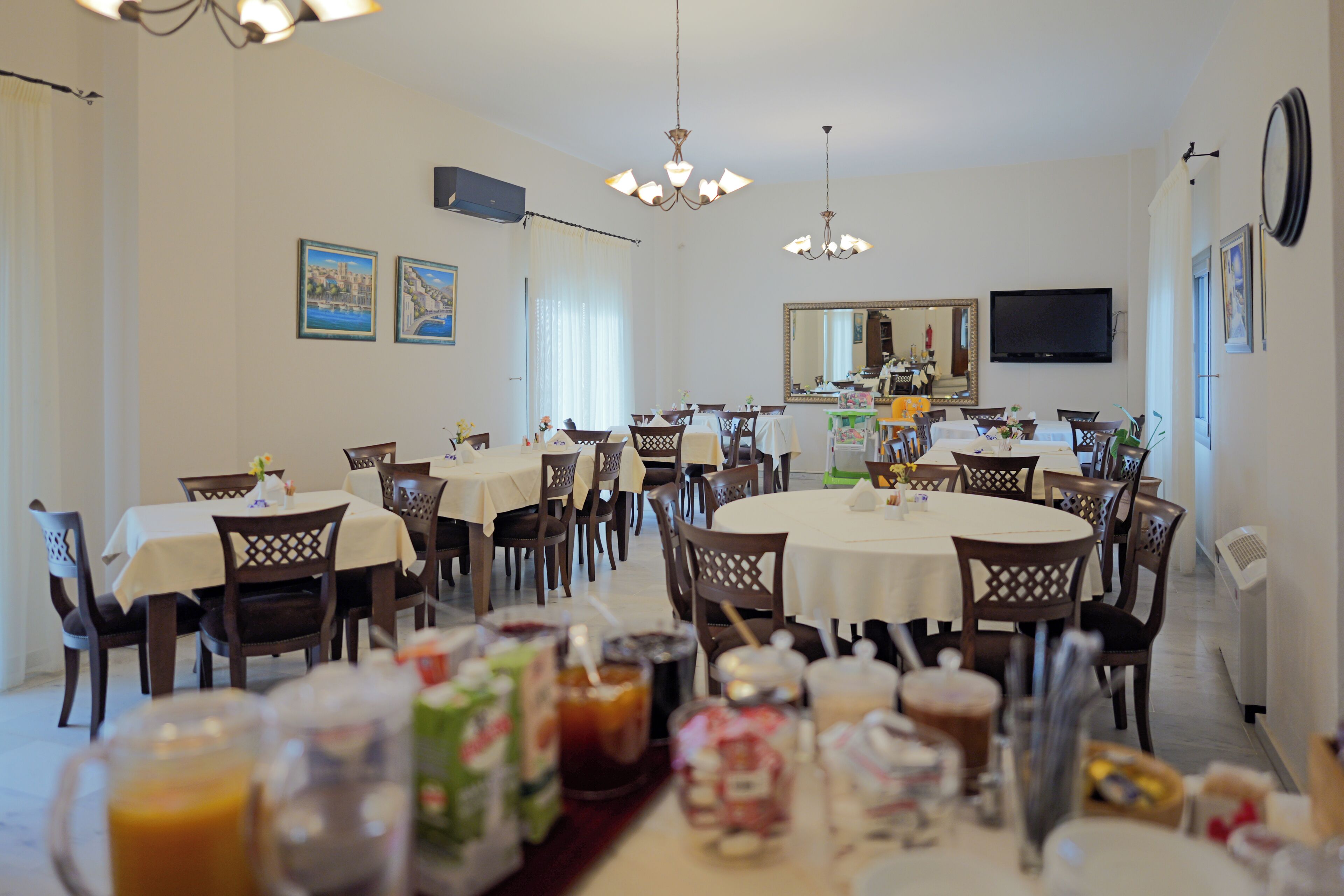 A dining area with multiple tables and chairs, a chandelier, and a television mounted on the wall.