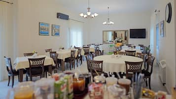 A dining area with multiple tables and chairs, a chandelier, and a television mounted on the wall.