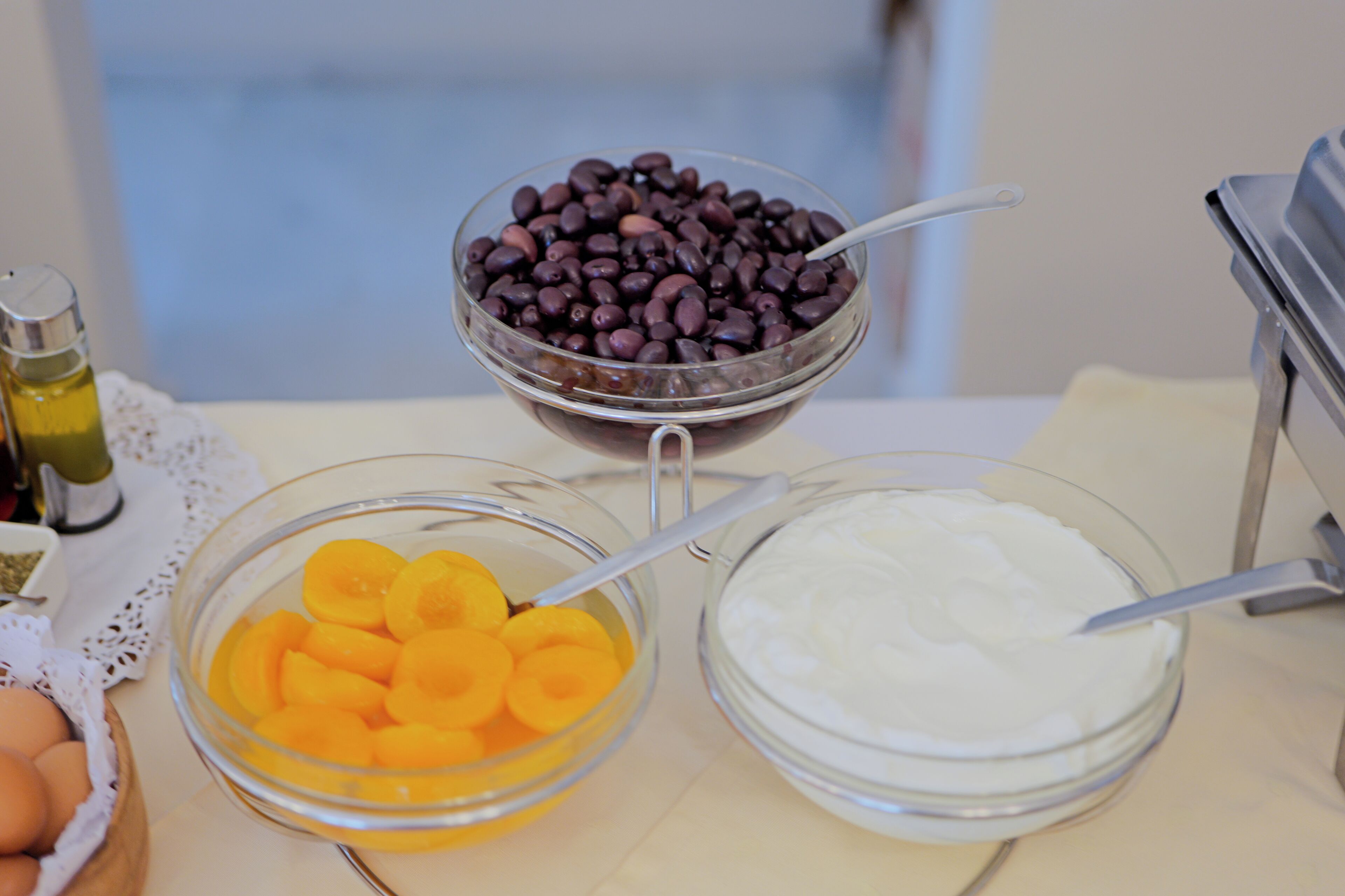 Three glass bowls containing different food items, a bottle of oil, and a white container on a table.