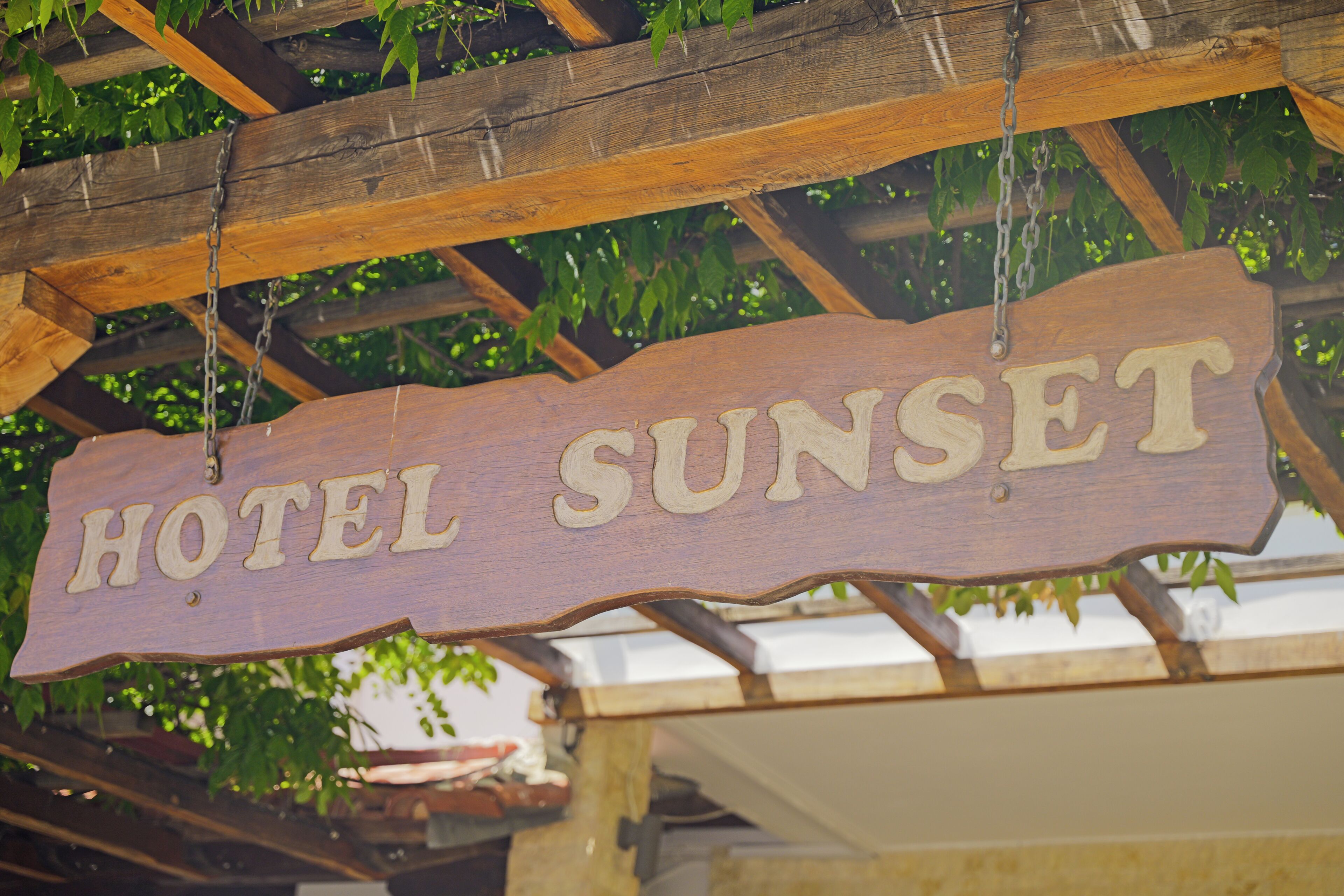 Uma placa de madeira com a inscrição 'HOTEL SUNSET' pendurada numa estrutura de madeira.