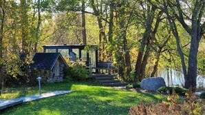 A rustic cabin with a wooden deck and a stone structure in a forested area.