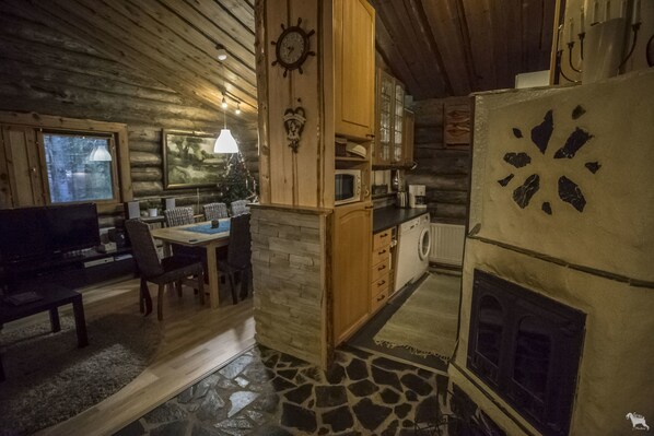 A cozy cabin interior with a stone fireplace, wooden walls, a dining area, and a kitchen with a microwave and cabinets.