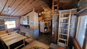 A rustic cabin interior with a stone fireplace, wooden ceiling beams, and a dining area with a striped table.