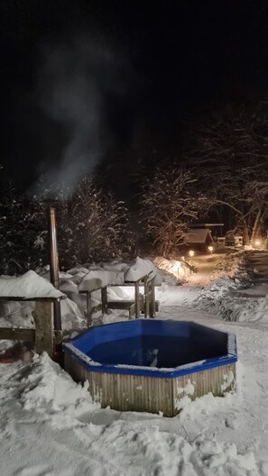 A snow-covered outdoor area with a hot tub, a wooden structure, and a small building in the background.