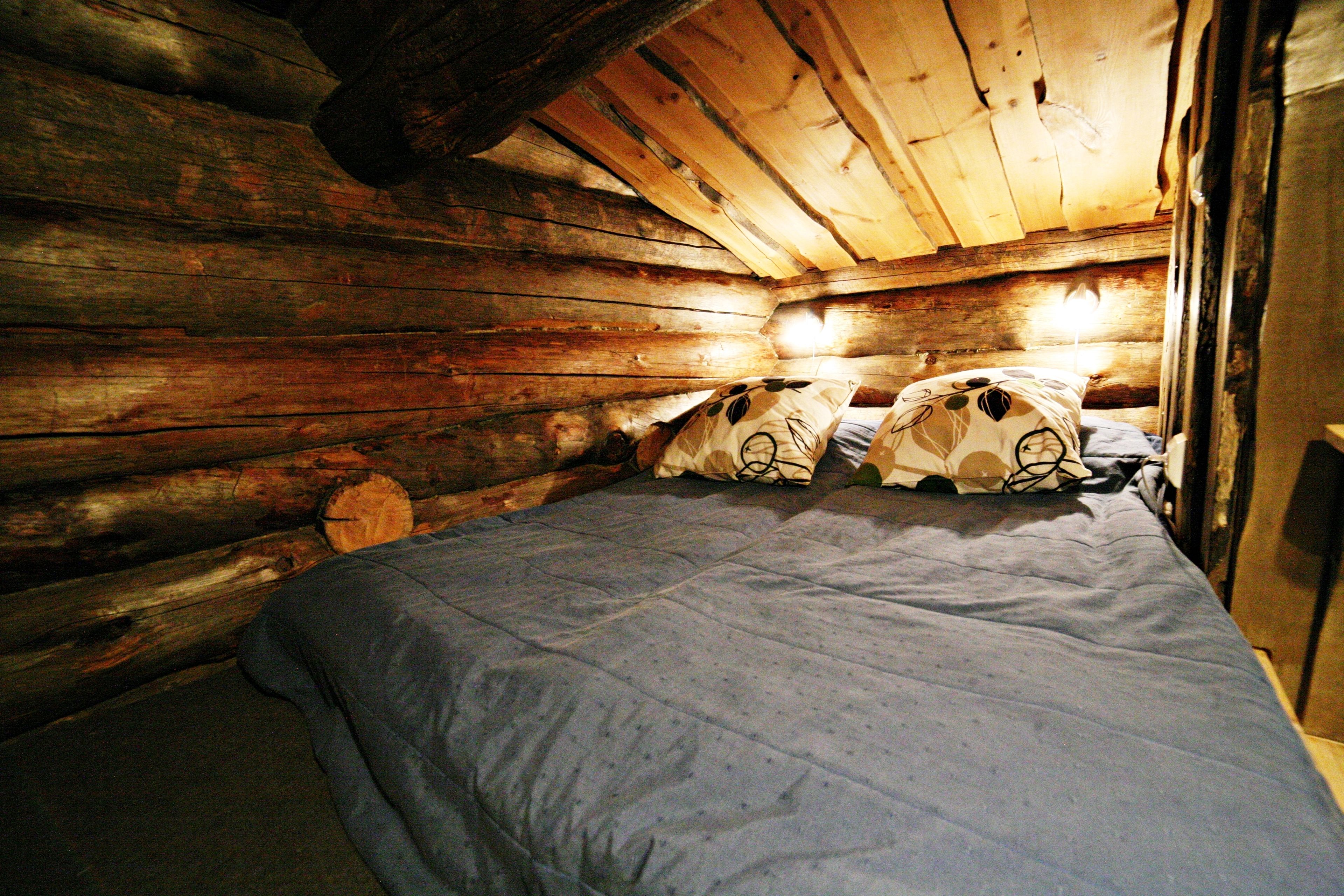 A wooden cabin bedroom with a bed, pillows, and a wooden ceiling.