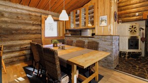 A rustic wooden interior with a dining area featuring a wooden table and wicker chairs, stone accents, and a fireplace.