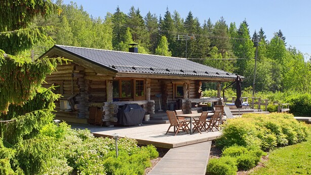 A log cabin with a deck, outdoor seating, and a view of a forested area.