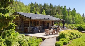 A log cabin with a deck, outdoor seating, and a view of a forested area. - Villa Kivikoski (Pyhtaa)