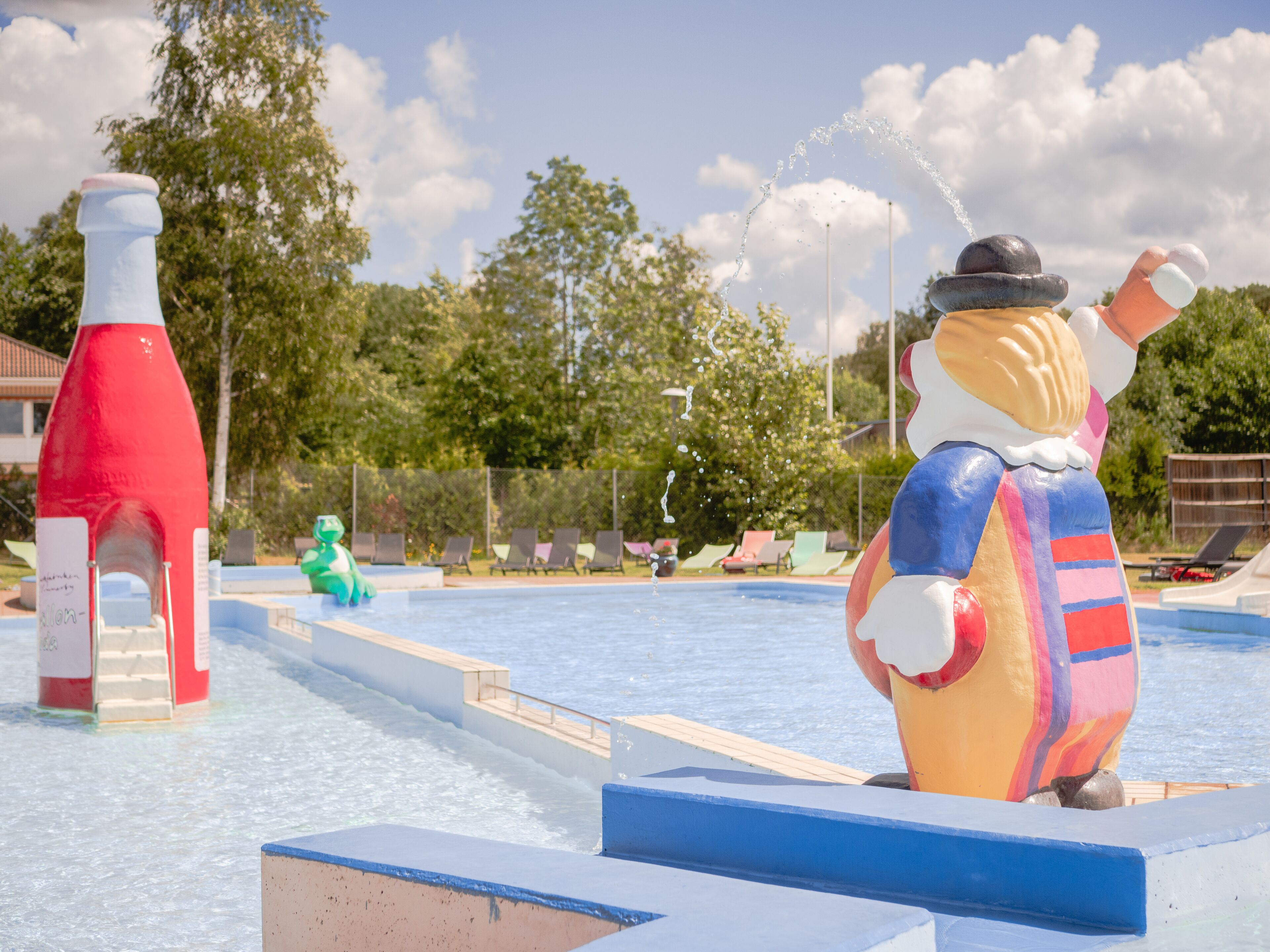 A water park with a large inflatable figure, a red water slide, and lounge chairs.