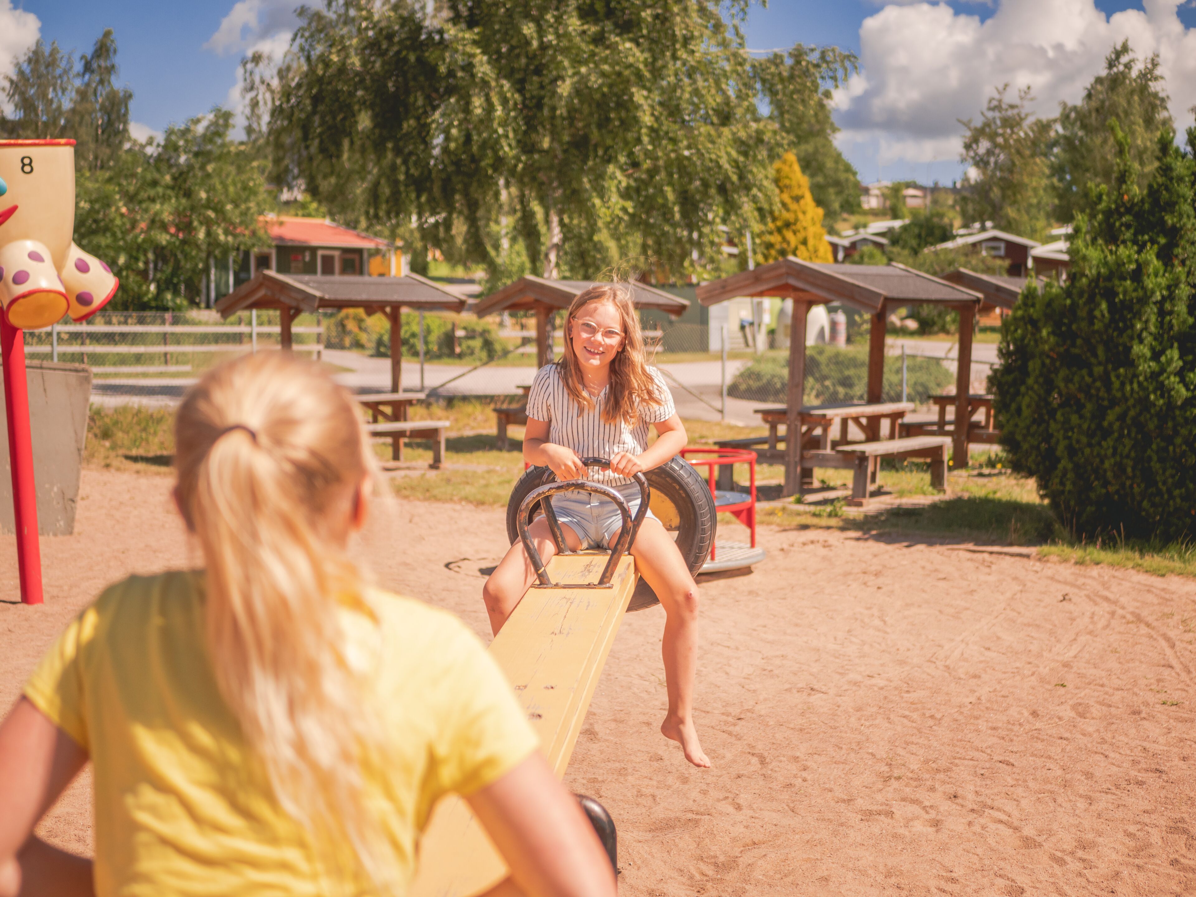 A playground with a seesaw, picnic tables, and a red and yellow structure.