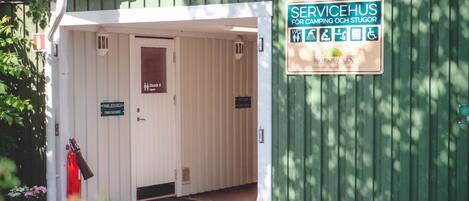 Un edificio verde con un letrero que indica que es una casa de servicios para camping y establos. Se ve una puerta con la leyenda "FAMILIEDUSCH" y un cartel para ducha familiar.