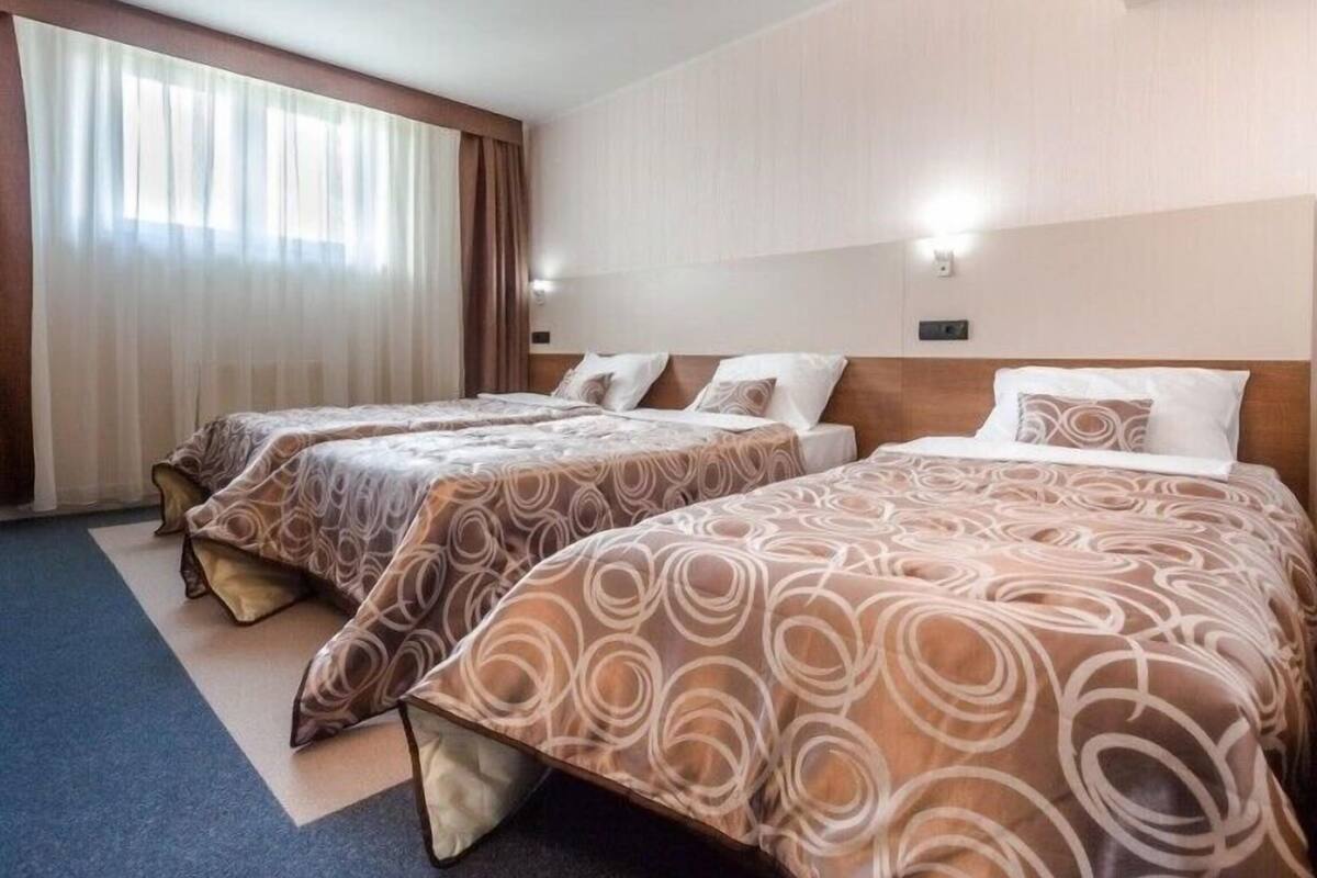 A hotel room with two beds, a large window with curtains, and a headboard with a light fixture.