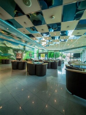 A spacious lobby with a modern ceiling design, multiple seating areas, and a large screen displaying a nature scene. - Hotel Macola (Plitvicka Jezera)