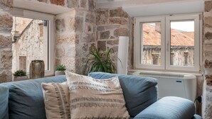 A cozy room with a stone wall, a blue sofa, and a view of red-roofed buildings through a window. - Villa Mirabilis, stunning superior villa, Dubrovnik Old Town (Dubrovnik)
