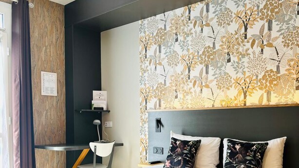 A modern hotel room with a large bed, a headboard with a floral pattern, a desk with a chair, and a window with curtains. - Hotel Le Castel Fleuri (Tours)