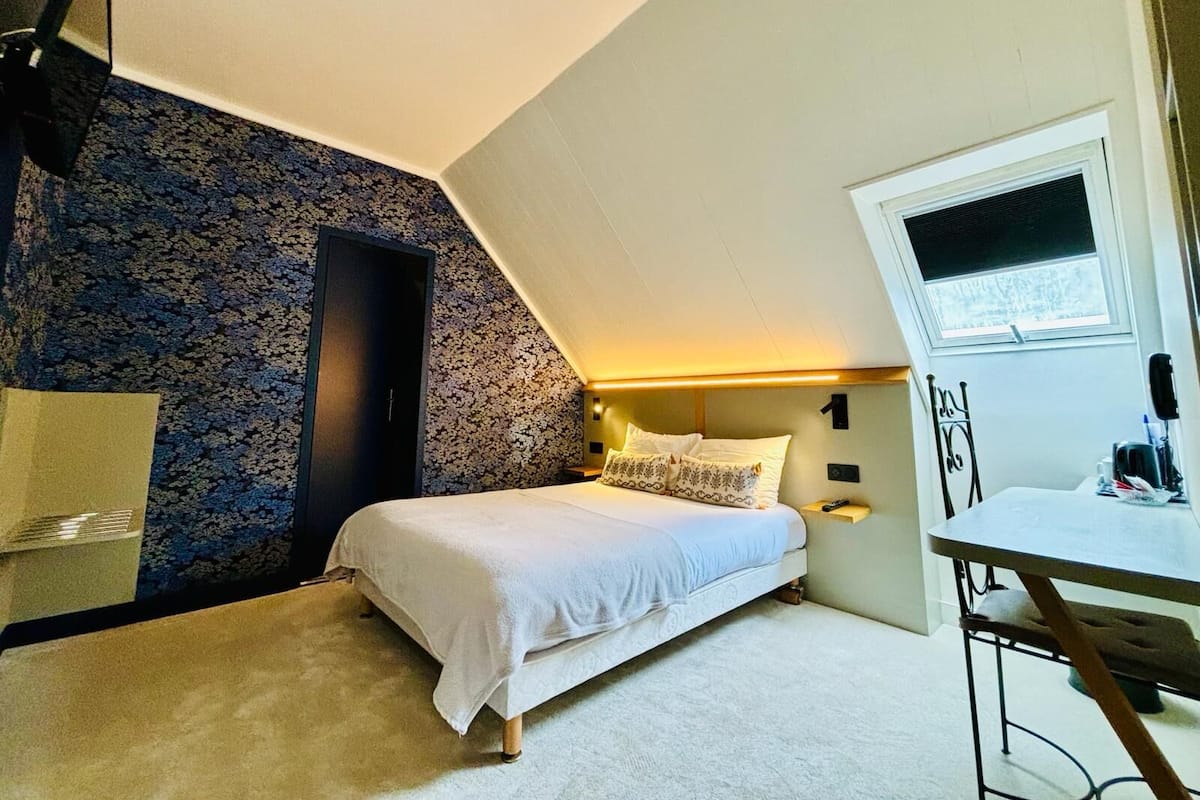 A bedroom with a bed, a desk, a chair, a window, and a door.