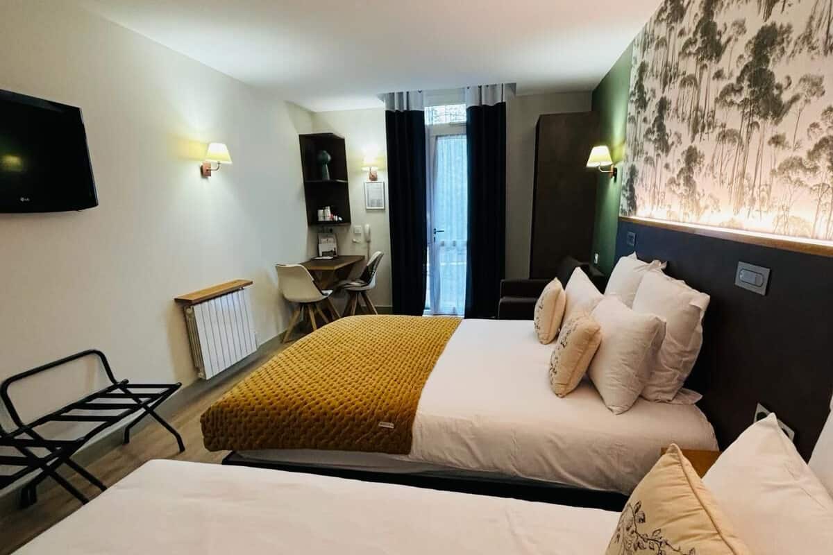 A hotel room with two beds, a desk, a chair, a TV, and a view of the outdoors.
