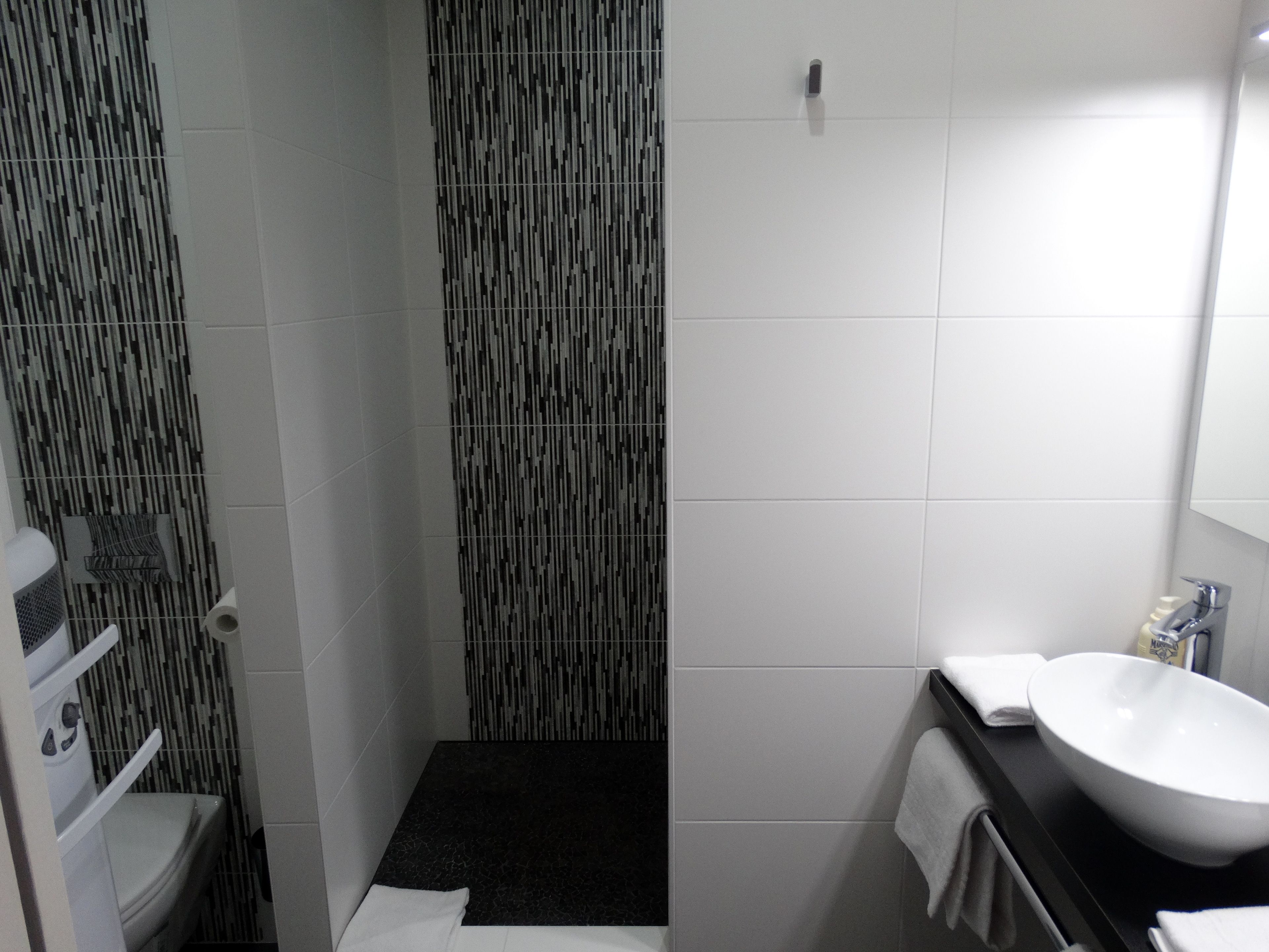 Un baño moderno con ducha de azulejos negros, lavamanos blanco y un perchero para toallas.