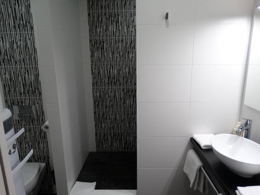 Un baño moderno con ducha de azulejos negros, lavamanos blanco y un perchero para toallas.