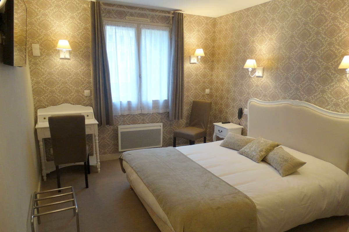 A hotel room with a bed, desk, chair, and two bedside lamps.