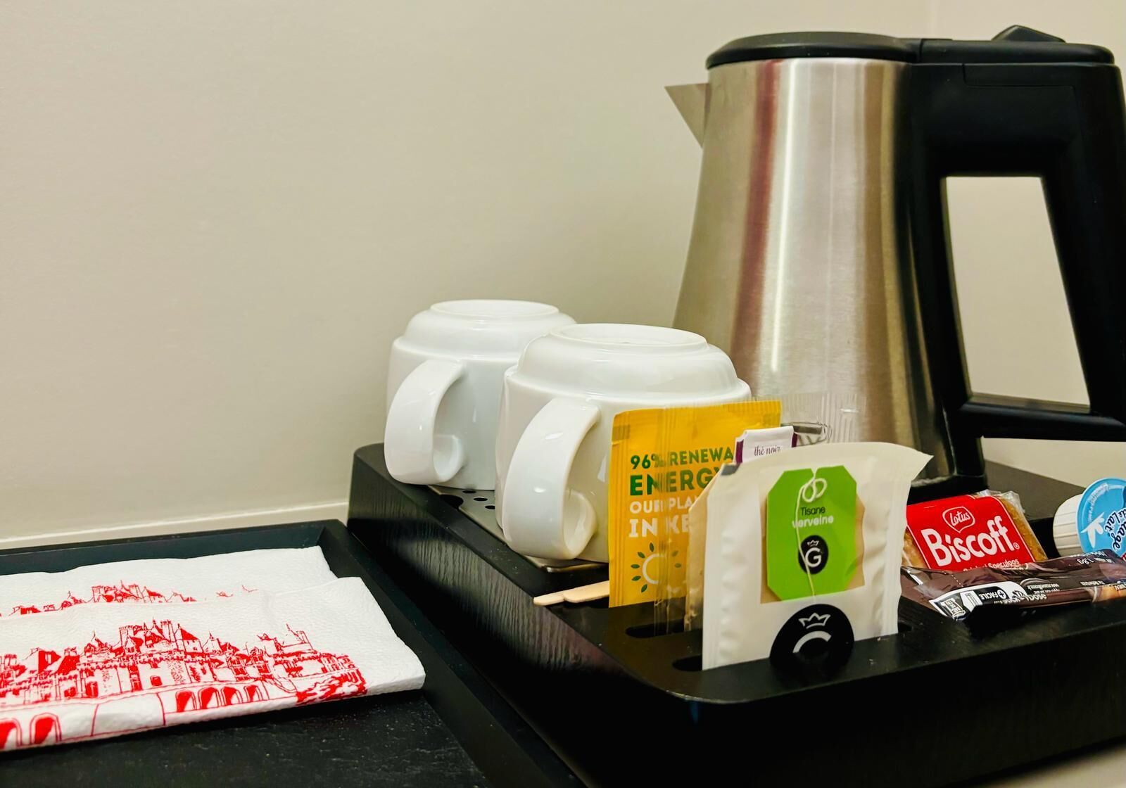 Un angolo caffè con una macchina da caffè, quattro tazze bianche, un vassoio con fazzoletti, una confezione di biscotti, una confezione di tisane e un’indicazione di energia rinnovabile al 96%.