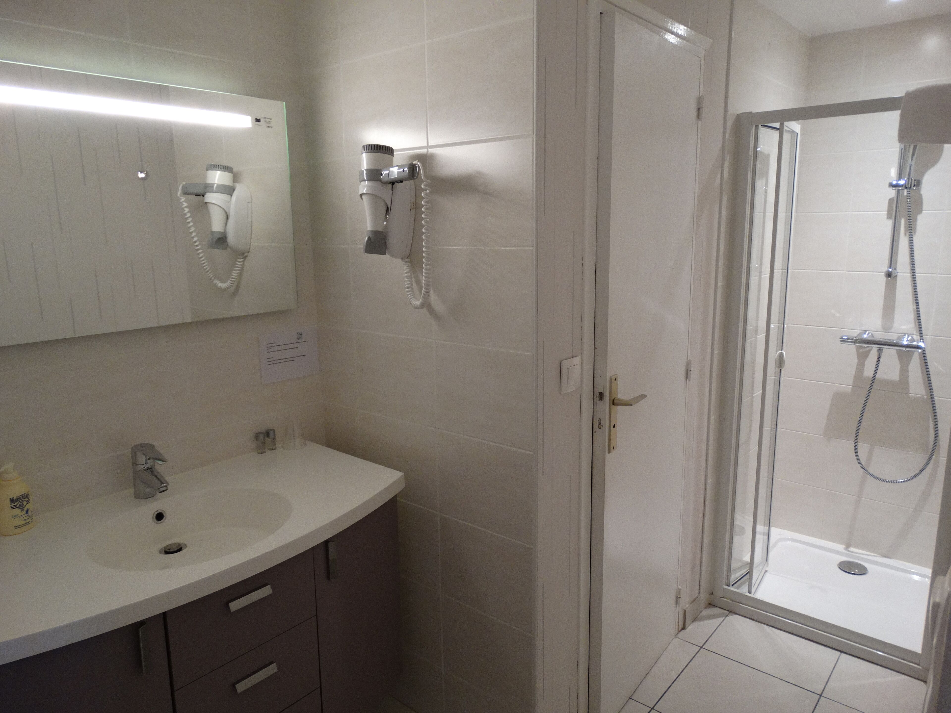 A bathroom with a sink, mirror, hairdryer, and shower.